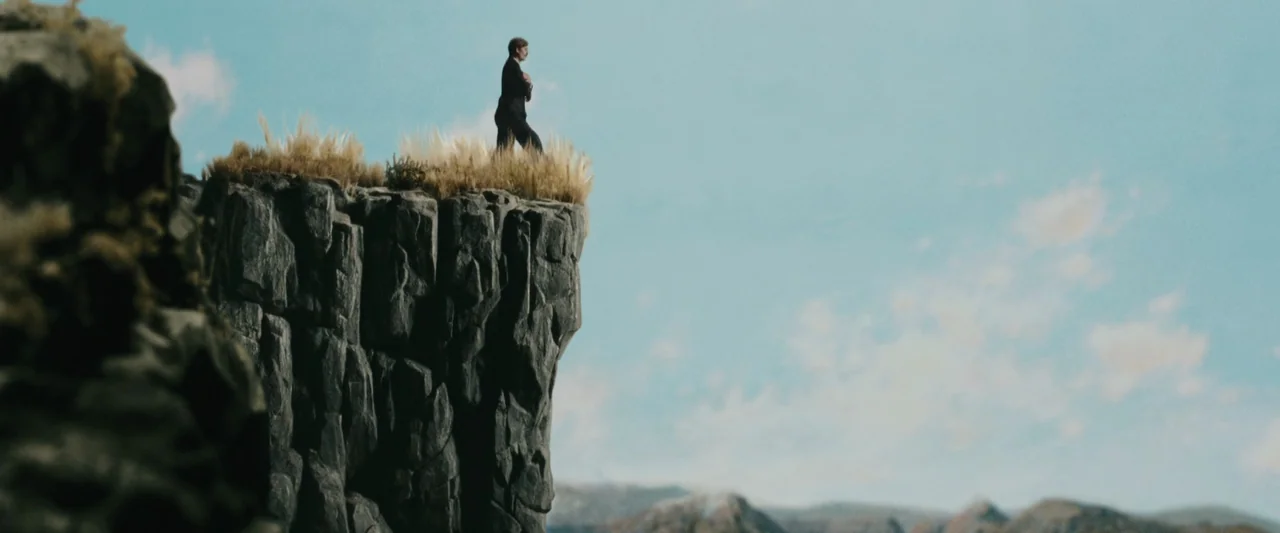Chicken With Plums (2011) movie still: wide — A high, jagged rock cliff rises against a light blue, hazy sky. A single man stands at the very edge…
