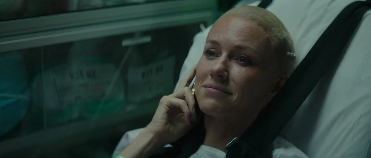 The Sea of Trees (2015) movie still: closeup — A woman lies on a hospital bed in a dimly lit room with medical equipment. She is resting her head on…