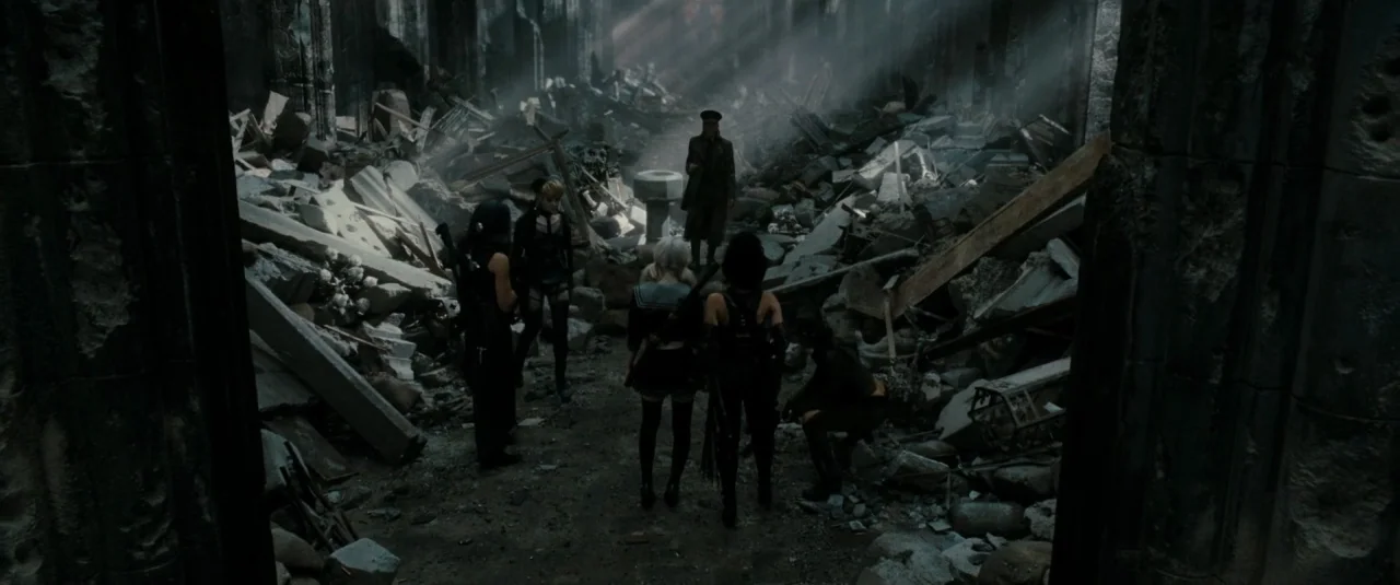 Sucker Punch (2011) movie still: wide — A destroyed stone interior space filled with large debris and structural ruins. A group of women faces a man…