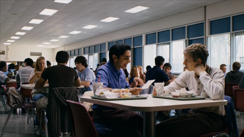 Youth In Revolt (2009) movie still: wide — A crowded school cafeteria with rows of tables and large windows. Two teenagers sit at the foreground…