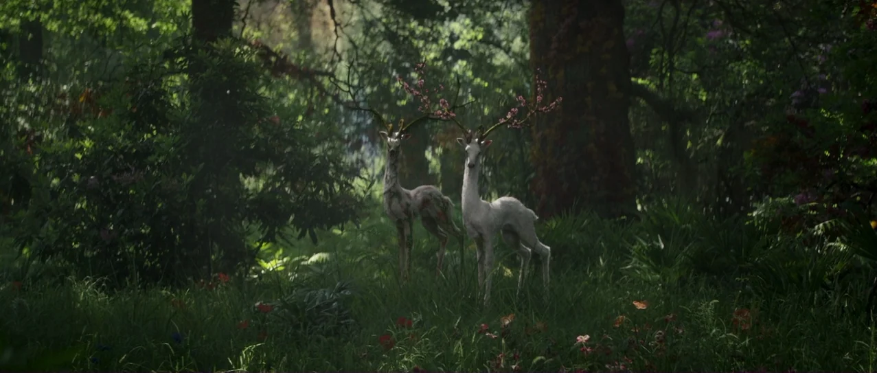 Annihilation (2018) movie still: wide — A lush green woodland clearing is filled with tall grass and vibrant flowering plants. Two slender white…