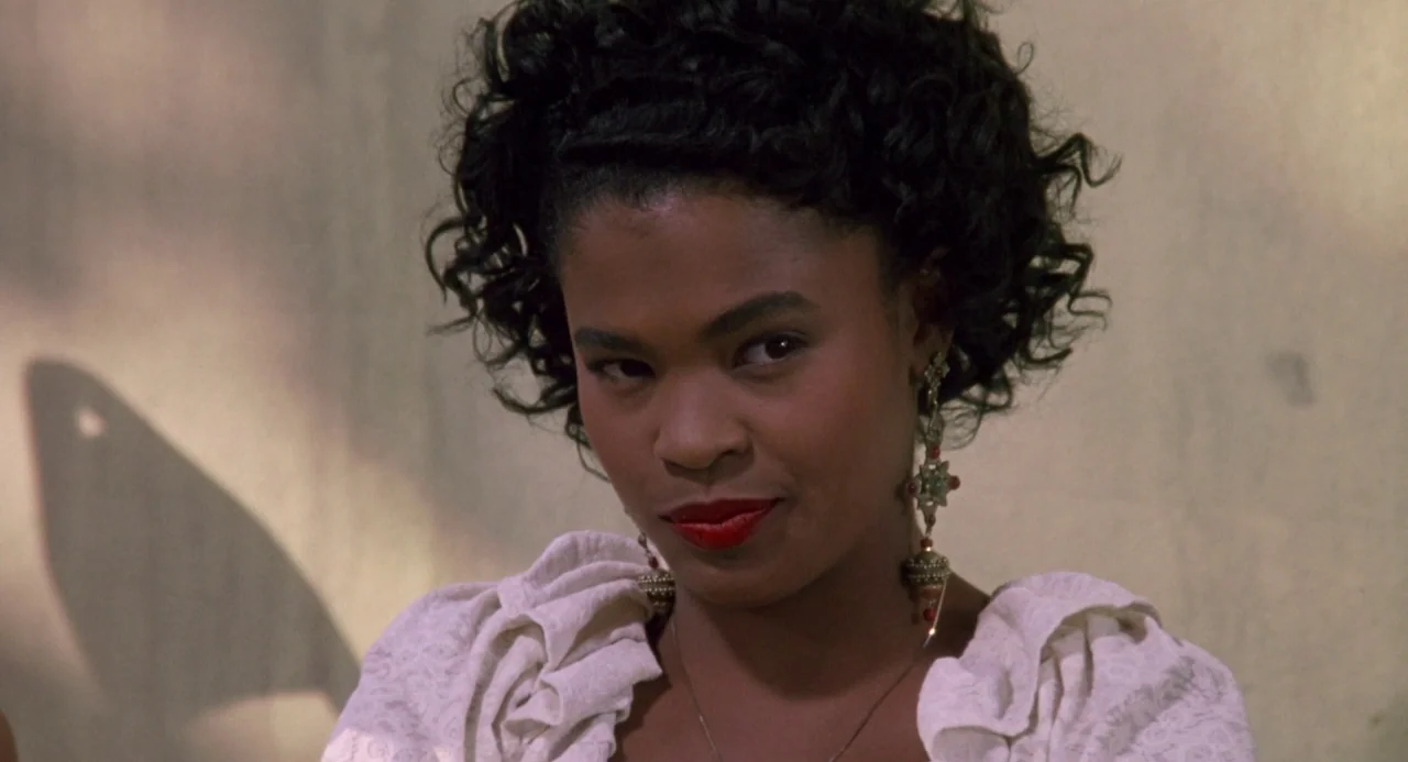 Boyz In The Hood (1991) movie still: closeup — A woman stands before a light beige wall with a distinct shadow pattern. She looks directly at the…