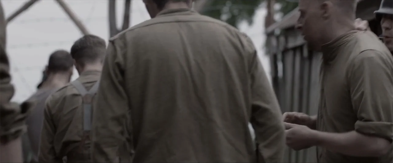 Behind the Line: Escape to Dunkirk (2020) movie still: medium — A group of men in tan 1940s-style military uniforms stand together outdoors. The…