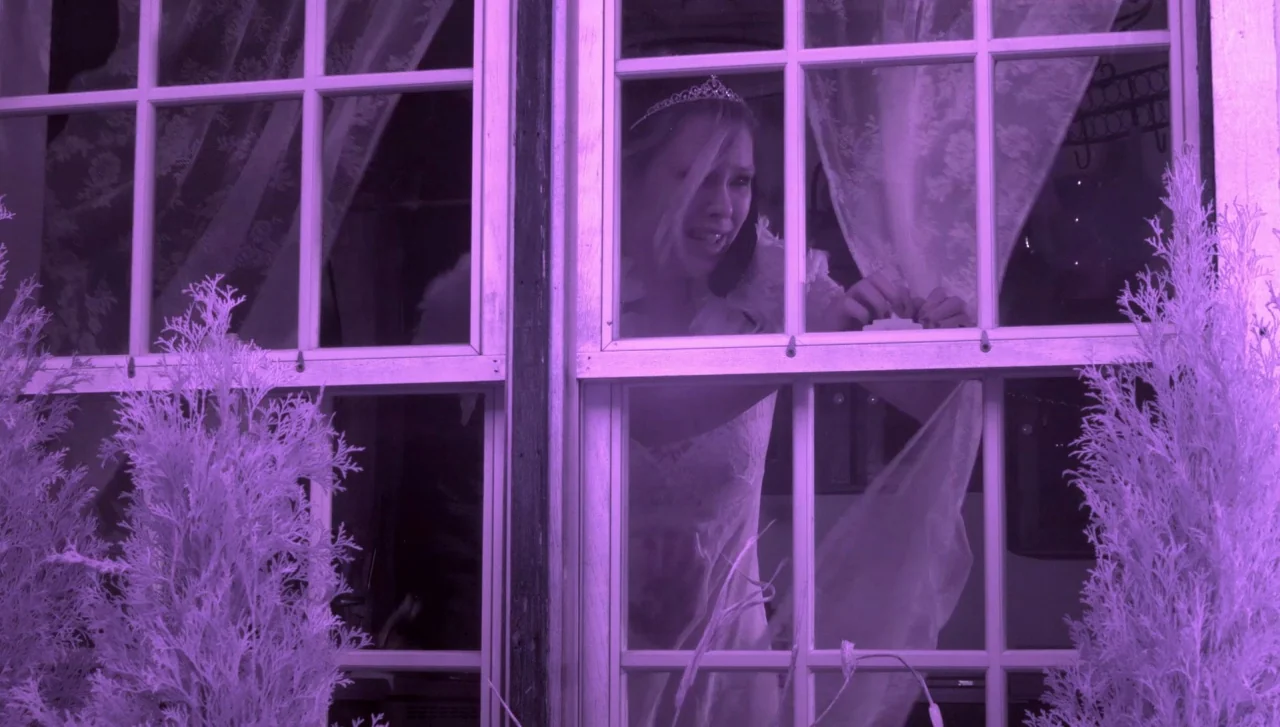 Hellions (2015) movie still: medium — A woman stands behind a multi-pane glass window at night. She grips a white lace curtain with her hand while…