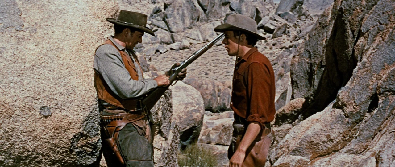 Comanche Station (1960) movie still: fullbody — A rugged desert landscape features large weathered rock formations and sparse dry vegetation. Two…