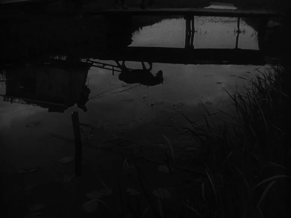 Sawdust and Tinsel (1953) movie still: wide — A dark pond surface mirrors the silhouette of a wooden bridge and carriage. The frame is inverted to…