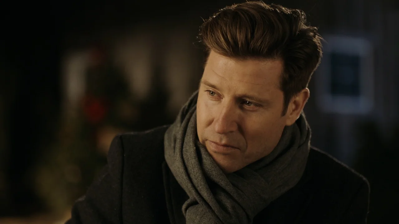 Christmas in Washington (2003) movie still: closeup — A dark indoor space features a man in winter clothing with a blurred background. The man gazes…