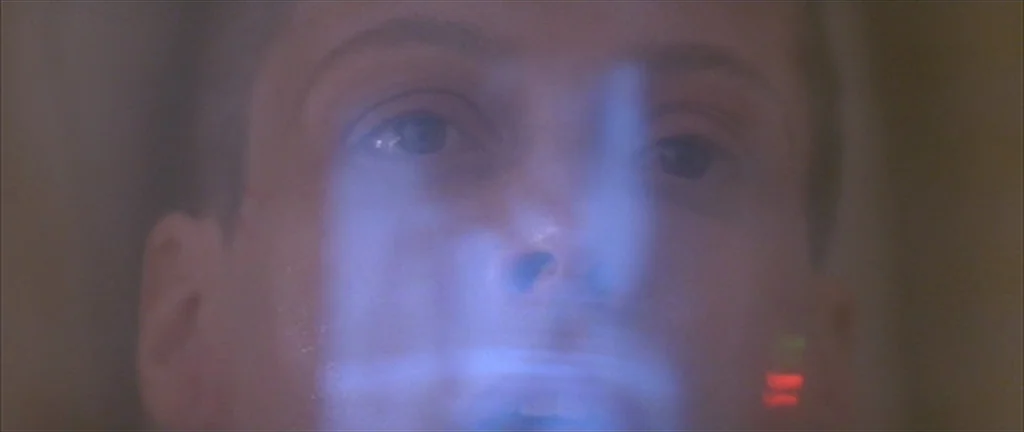 Alien 3 (1992) movie still: closeup — A man's face is shown in close-up against a blurred background. The subject is lit by the blue screen of a…