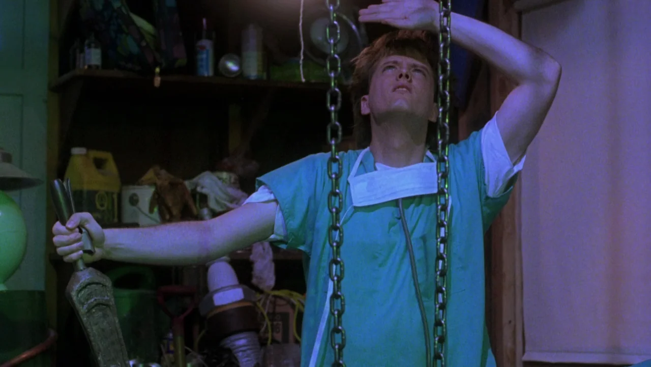 Frankenhooker (1990) movie still: medium — A cluttered garage contains stacked containers, tools, and miscellaneous hardware on wooden shelves. A…