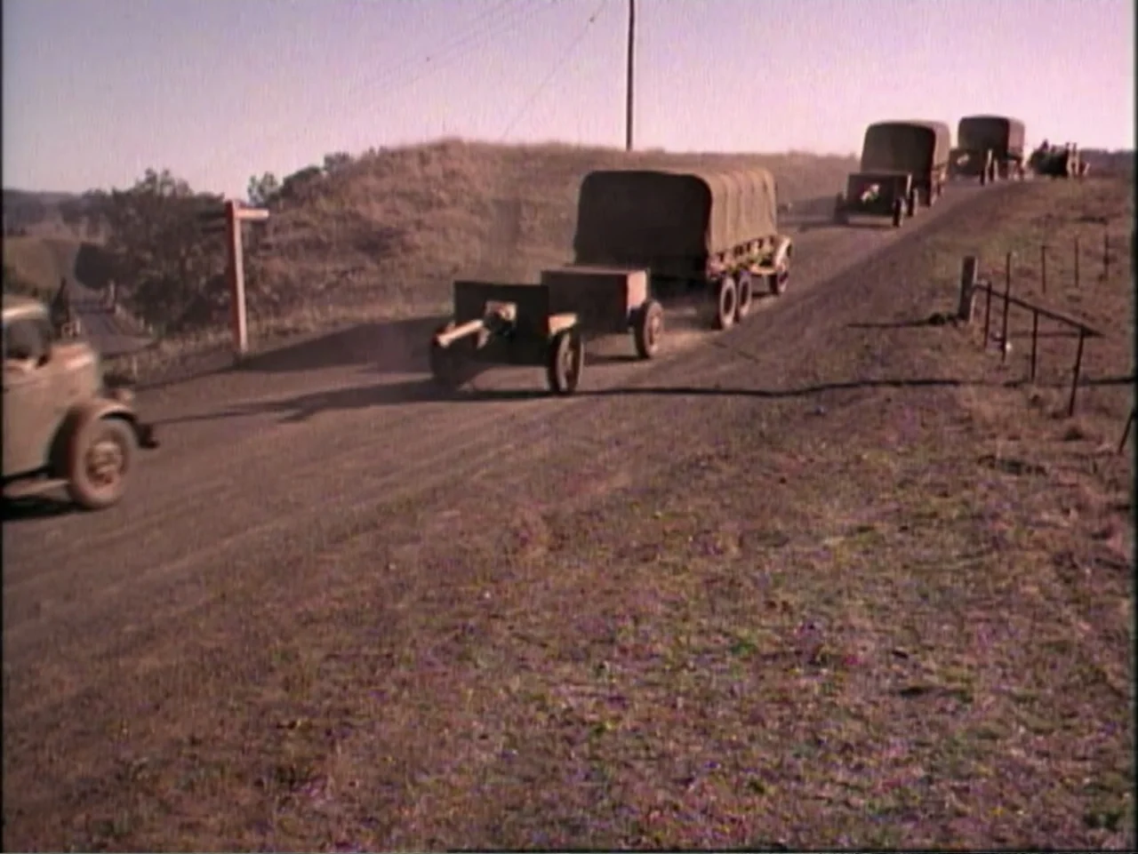In Pursuit of Honor (1995) movie still: wide — A convoy of vintage military trucks travels along a dusty rural dirt road. The vehicles kick up dust…