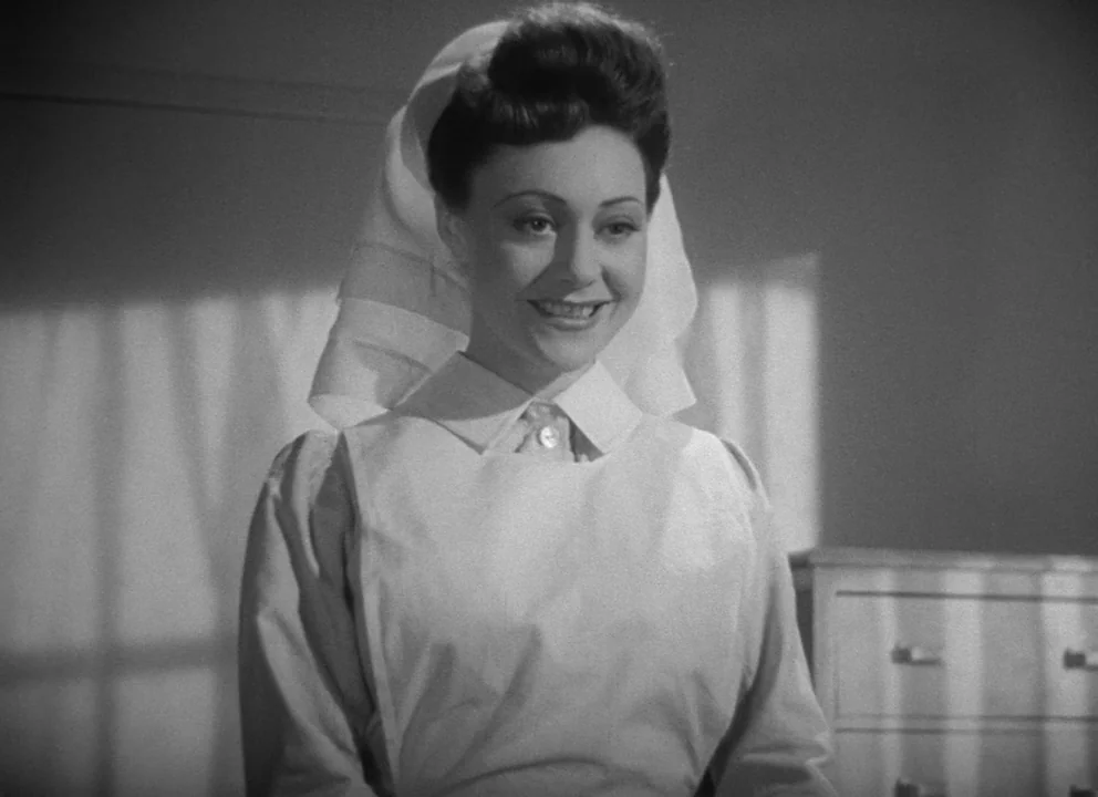 Dead of Night (1945) movie still: medium — A hospital interior with a wooden chest of drawers visible in the background. A young woman dressed in a…