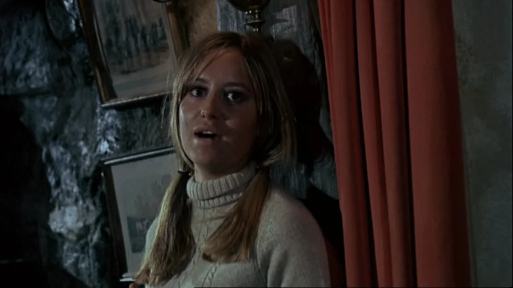 Straw Dogs (1971) movie still: medium — An interior space features textured walls adorned with framed pictures and vibrant orange curtains. A woman…