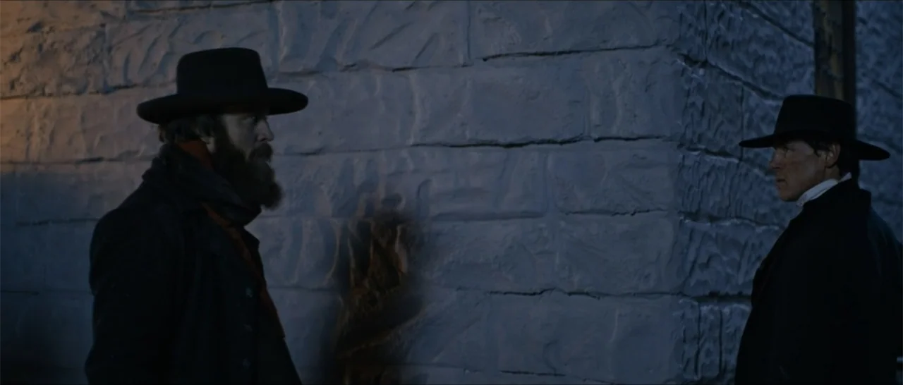 Out of Liberty (2019) movie still: medium — Two men stand outdoors at night beside a rough-hewn stone wall. The pair face each other in profile…