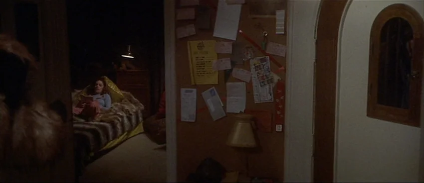 California Split (1974) movie still: wide — A dark hallway connects to a bedroom visible through an open doorframe. A young woman lies in bed…