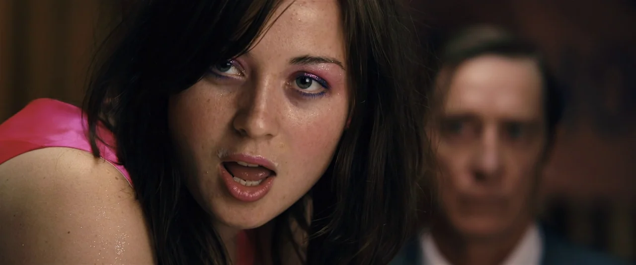 The Loved Ones (2009) movie still: closeup — A dimly lit interior space contains a young woman and an out-of-focus man. The woman has iridescent…