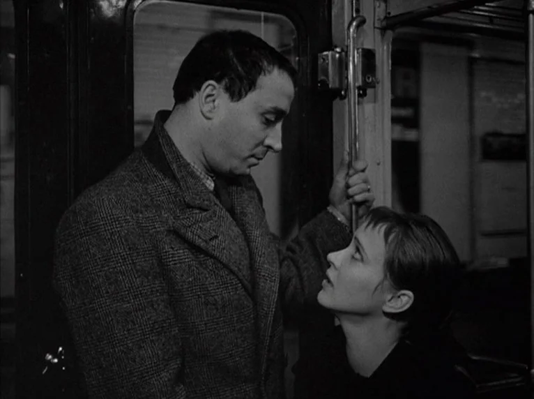 Band of Outsiders (Bande à part) (1964) movie still: medium — A dark, cramped interior space with a metallic grab rail and window frames. A man and…