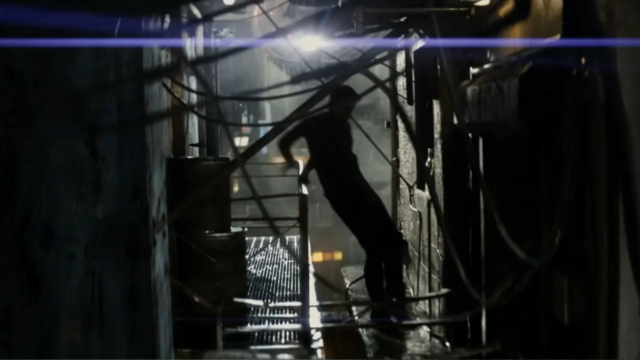 Total Recall (2012) movie still: medium — A metal fire escape at night with tangled cables and distant city lights. A man stands in silhouette…