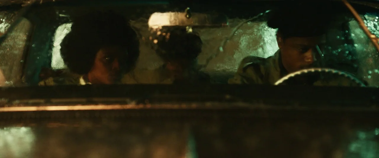 Judas and the Black Messiah (2021) movie still: medium — The interior of a moving vintage car during a heavy nighttime rainstorm. Three individuals…