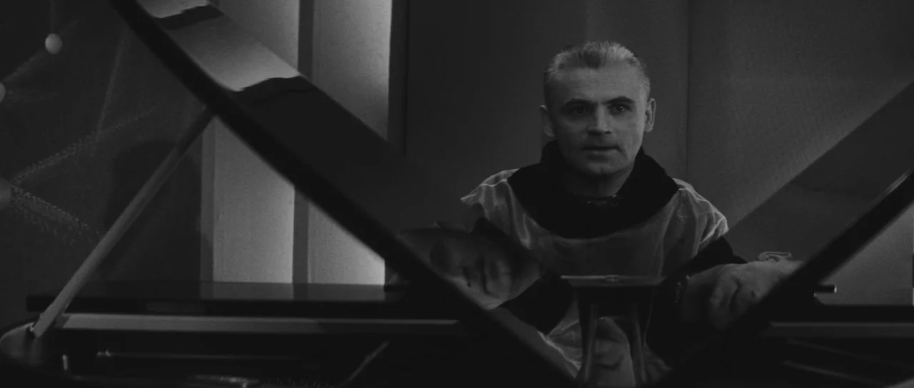 Ikarie XB 1 (1963) movie still: medium — An interior space features a man sitting behind the lid of a grand piano. The dark instrument reflects the…