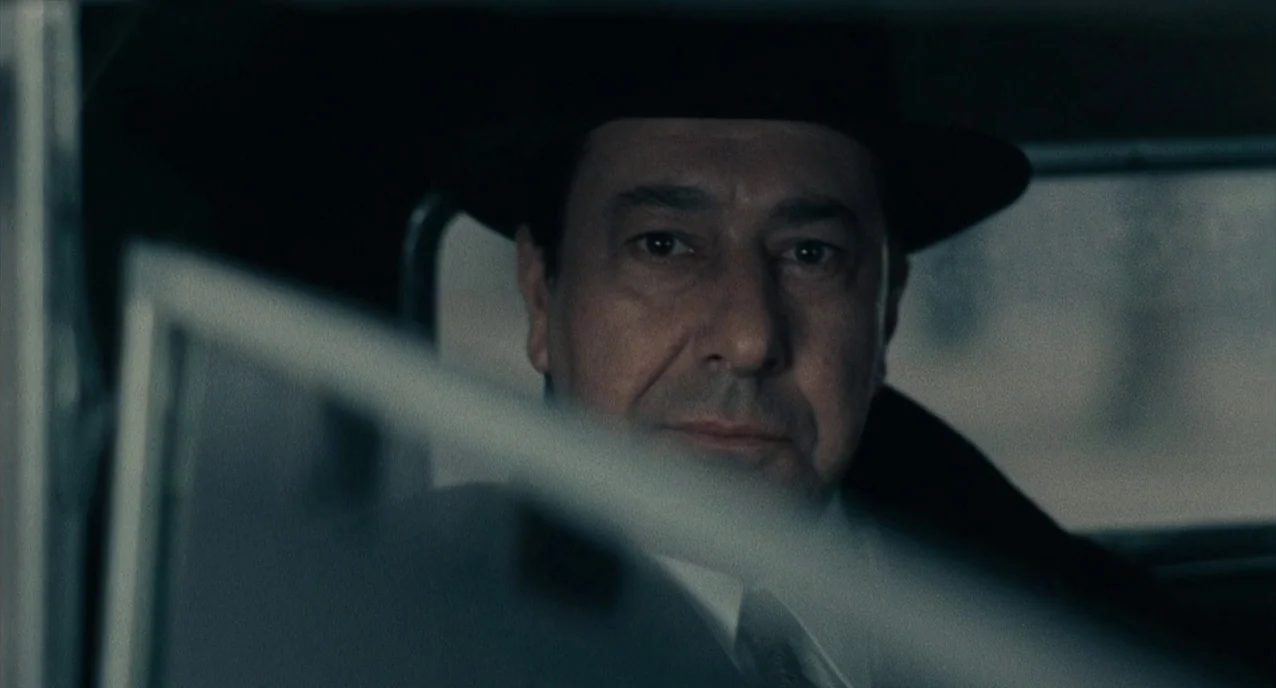 The Army of Shadows (1969) movie still: closeup — A man sits inside a vehicle with his face framed by the windshield frame. He looks toward the…