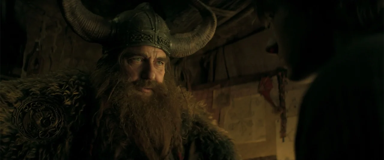 How to Train Your Dragon (2025) movie still: medium — A dimly lit tent interior features a man wearing a large horned metal helmet. A bearded man in…