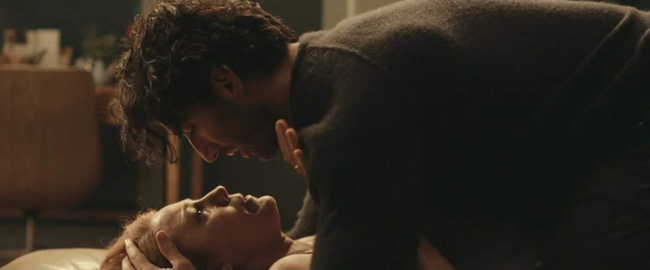 It Ends with Us (2024) movie still: medium — A dimly lit room with muted wall tones and soft interior surfaces. A man leans over a woman, his hands…