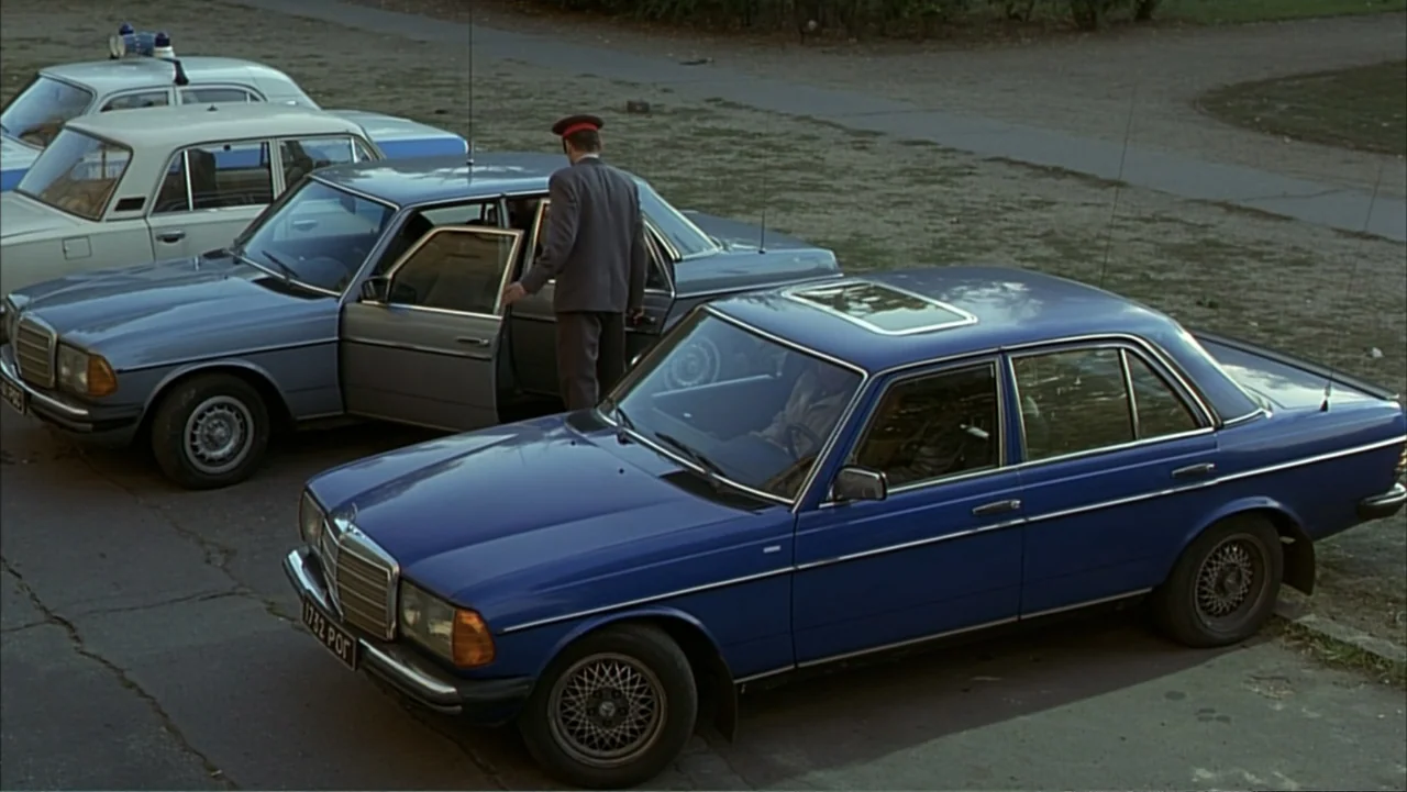 Citizen X (1995) movie still: wide — A paved lot contains multiple older European sedans parked under overcast daylight conditions. A man in a dark…
