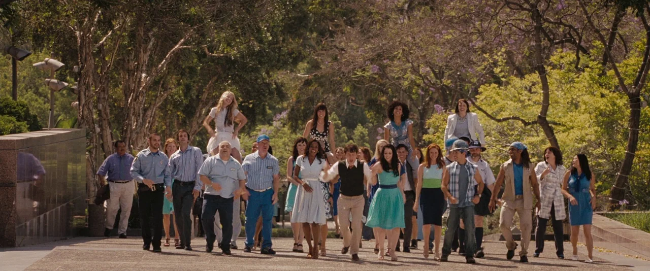 500 Days of Summer (2009) movie still: wide — A group of diverse individuals strolls along a wide paved pathway in a park. Many people wear casual…
