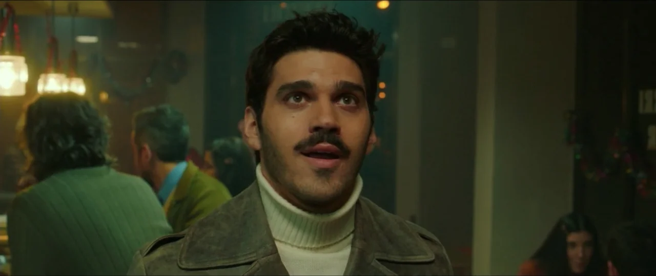 My Heart Goes Boom! (2020) movie still: medium — A dimly lit indoor space with blurred background figures suggesting a public eatery. A man in a…