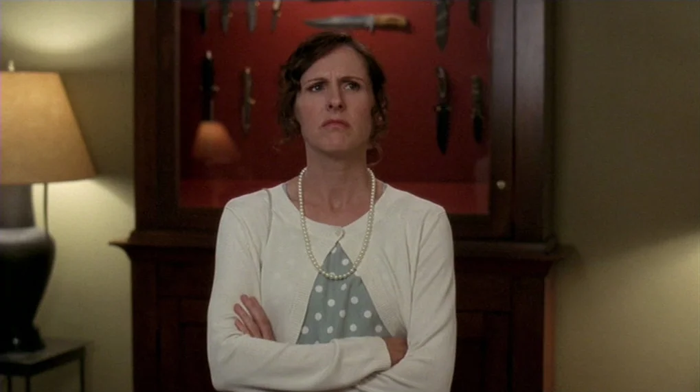 Year Of The Dog (2007) movie still: medium — A woman stands in front of a wooden cabinet containing a collection of knives. She is positioned…