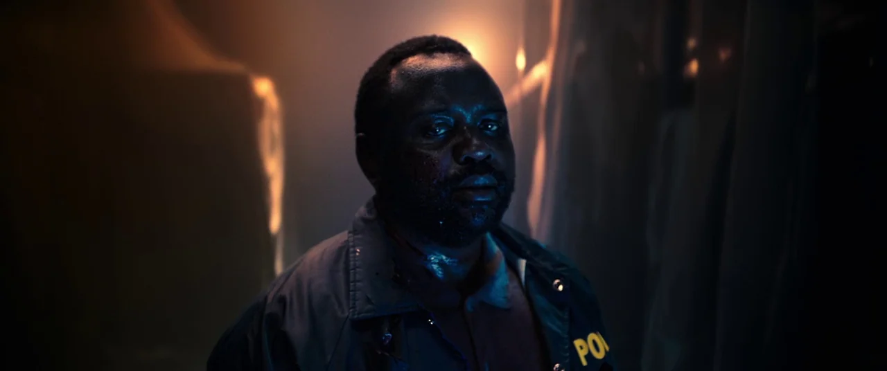 Child's Play (2019) movie still: closeup — A dark, smoke-filled space with indistinct shapes and surfaces in the background. A man wearing a police…