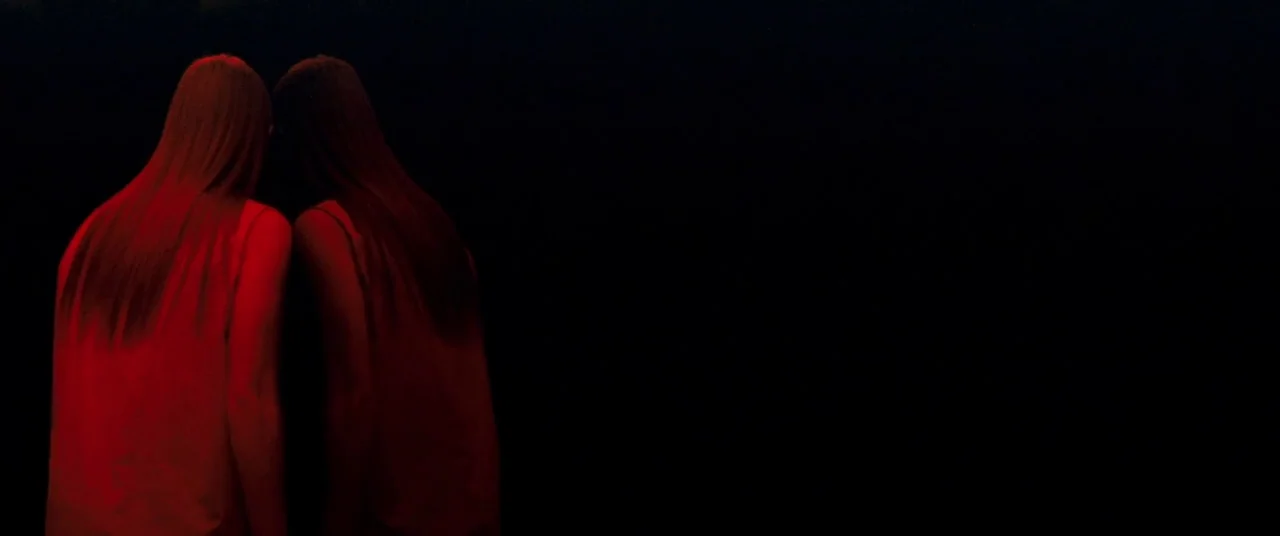 Beyond The Black Rainbow (2010) movie still: medium — A woman stands in a dark space before a large wall mirror. She stares at her own reflection in…