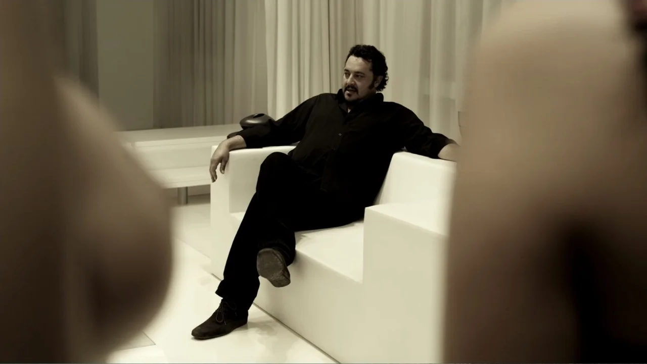 Assassination Games (2011) movie still: medium — A minimalist white lounge with a stark sofa and translucent white curtains. A man in black clothing…