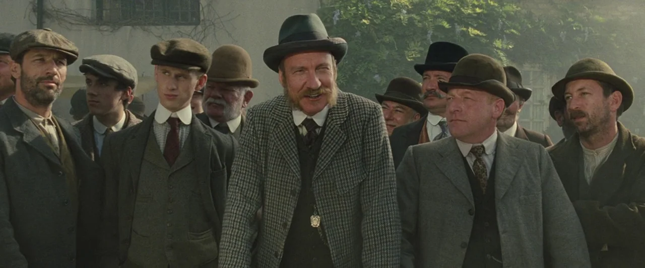 War Horse (2011) movie still: medium — A group of men in early 20th century attire stand together outdoors. The background shows a light-colored…