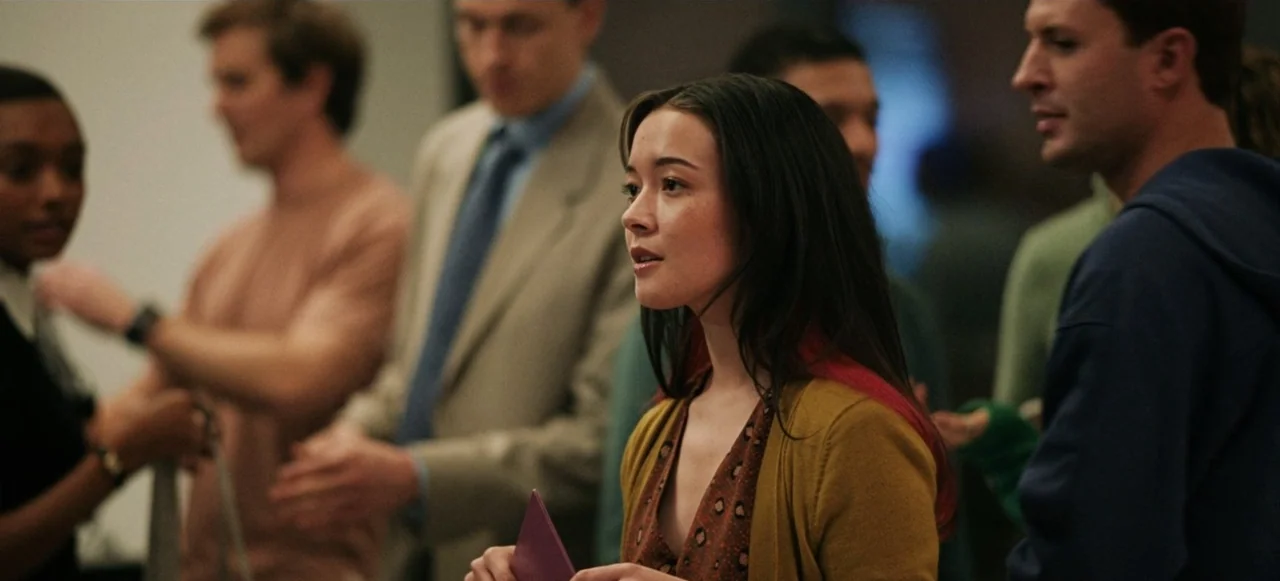 Babygirl (2024) movie still: medium — A group of diverse people stand in a dimly lit indoor event space. A woman in the foreground looks toward her…