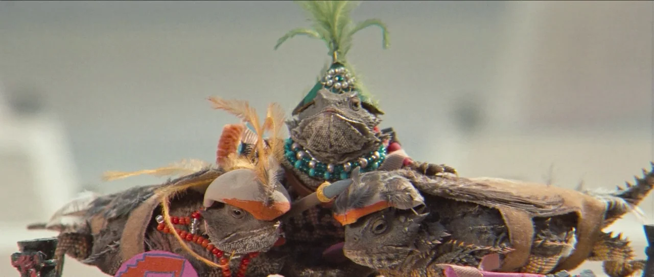 The Holy Mountain (1973) movie still: closeup — Three horned lizards wearing elaborate miniature costumes are positioned close together in an…