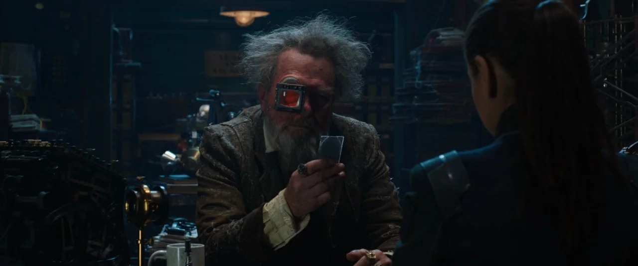 Jupiter Ascending (2015) movie still: medium — A dimly lit, cluttered workshop filled with mechanical parts and vintage items. An elderly man with a…