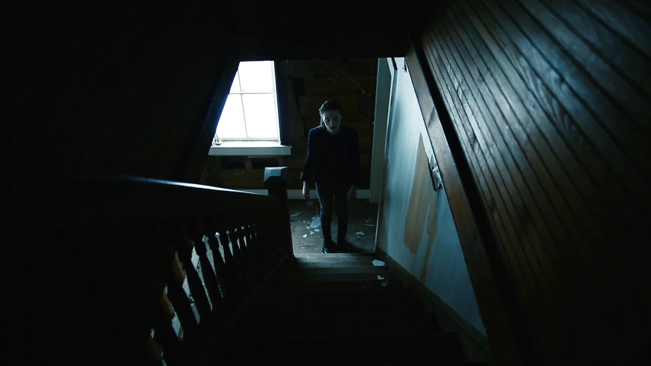 The Deeper You Dig (2019) movie still: medium — A dark, dilapidated upper floor with peeling paint and debris on the wood floor. A young woman…