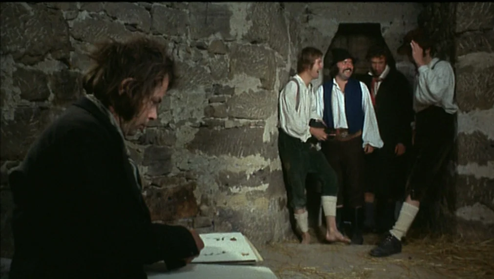 The Enigma Of Kaspar Hauser (1974) movie still: medium — A dark, rustic space features rough-hewn stone walls and a floor covered in straw. Five men…