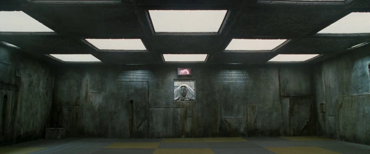 A Hitchhiker’s Guide To The Galaxy (2005) movie still: wide — A spacious, sterile concrete room features a checkered floor and recessed ceiling…