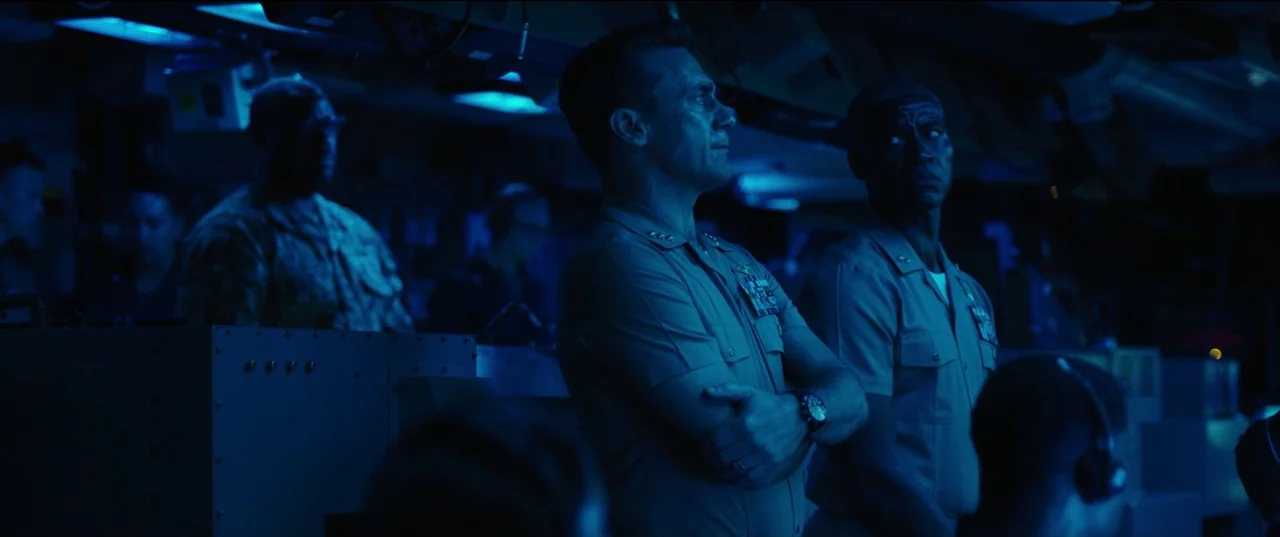 Top Gun: Maverick (2022) movie still: medium — A dark, cramped military control center filled with computer consoles and low blue light. Two navy…