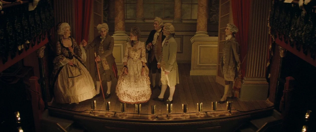 The Invisible Woman (2013) movie still: wide — A dimly lit 18th-century stage features ornate columns and draped red velvet curtains. Five actors in…