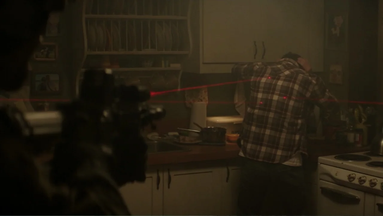 Skyscraper (2018) movie still: medium — A dark residential kitchen is filled with faint haze and cluttered countertops. A man in a flannel shirt…