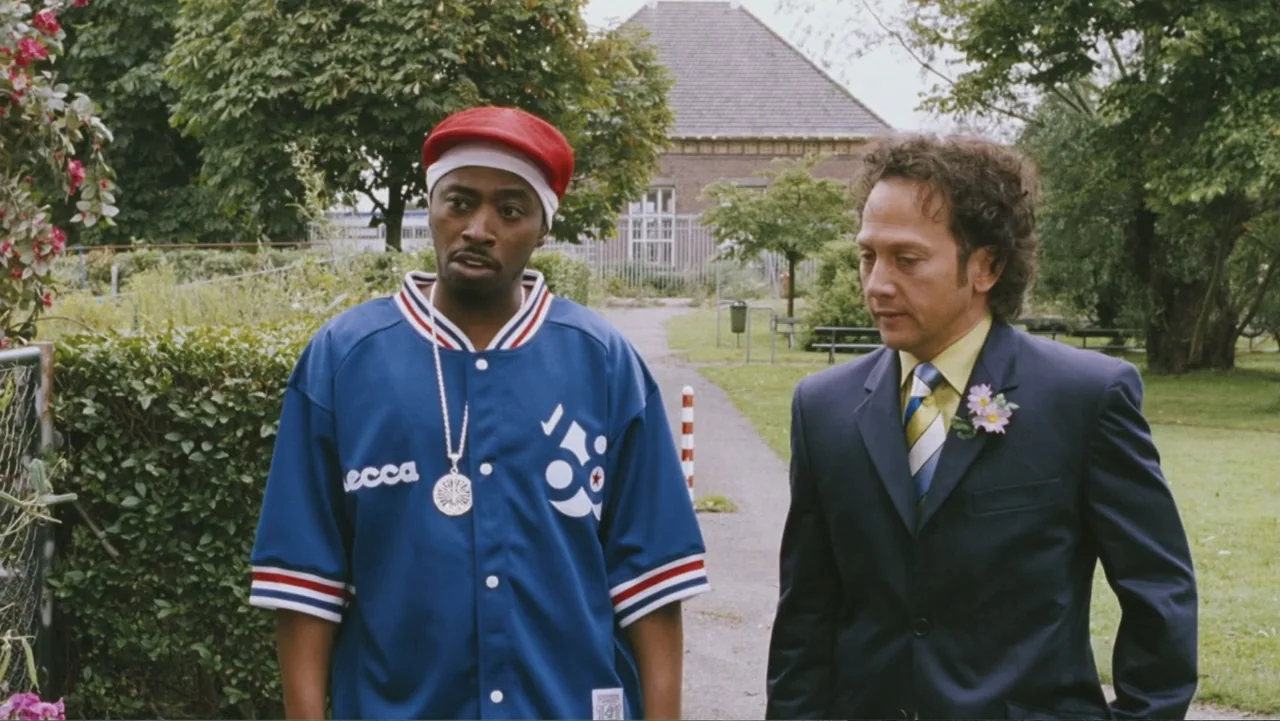 Deuce Bigalow: European Gigolo (2005) movie still: medium — A public park path features a man in a jersey and a suit-wearing man. The two men stand…