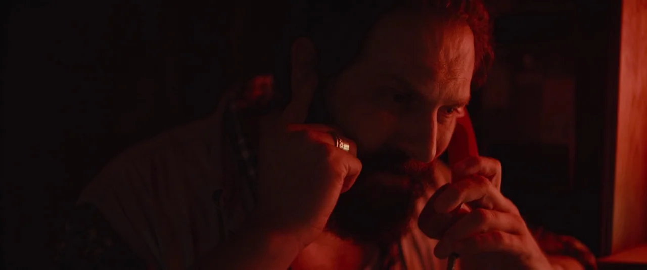 Blaze (2018) movie still: closeup — A man stands in a dark space filled with intense, monochromatic red light. He holds a vintage-style red…