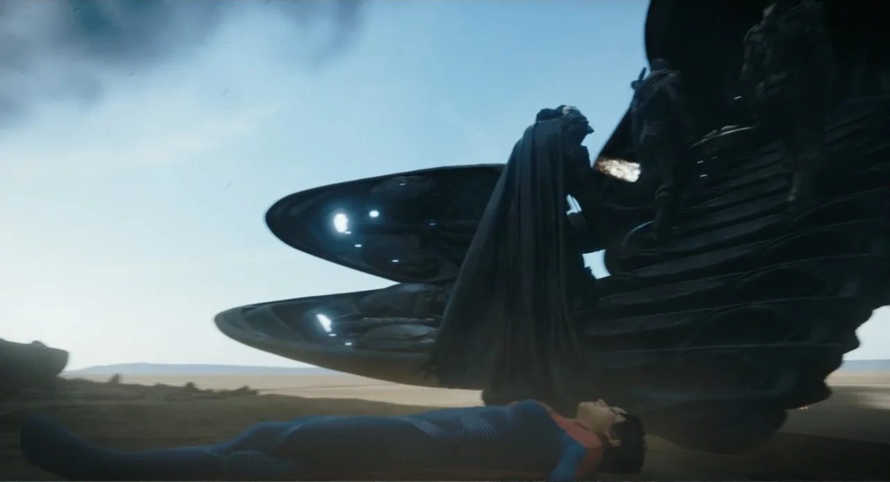 The Flash (2023) movie still: wide — A vast, empty desert landscape sits beneath a bright, overcast sky. A futuristic armored figure boards a large…