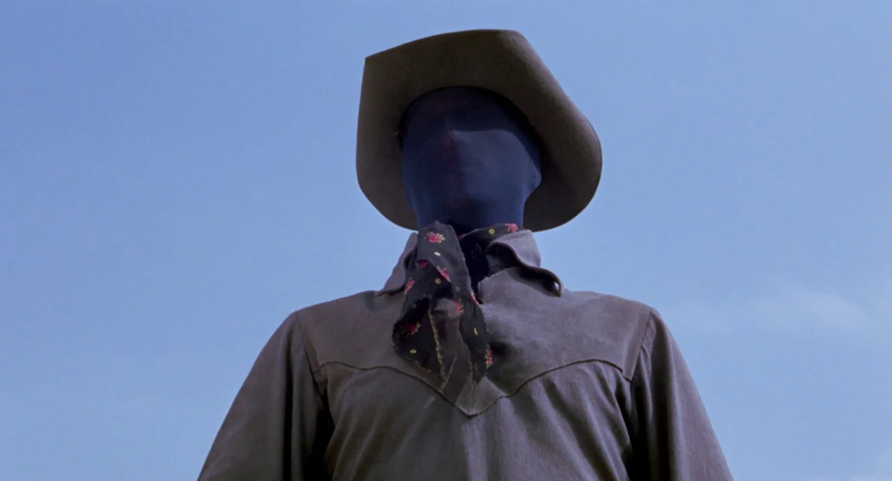 Johnny Colt (1966) movie still: medium — A figure stands in a vast, open outdoor space against a clear blue sky. The subject wears a brown hat and…