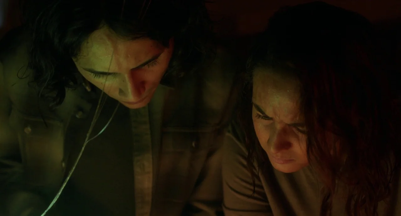 May The Devil Take You (2018) movie still: medium — Two individuals lean over a surface in a dark, enclosed space. They peer intently at a glowing…