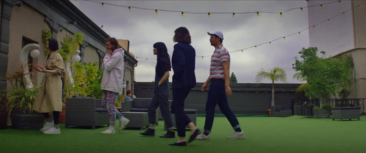 The Nowhere Inn (2020) movie still: fullbody — A rooftop terrace covered in artificial turf features a string of small lights above. Five…