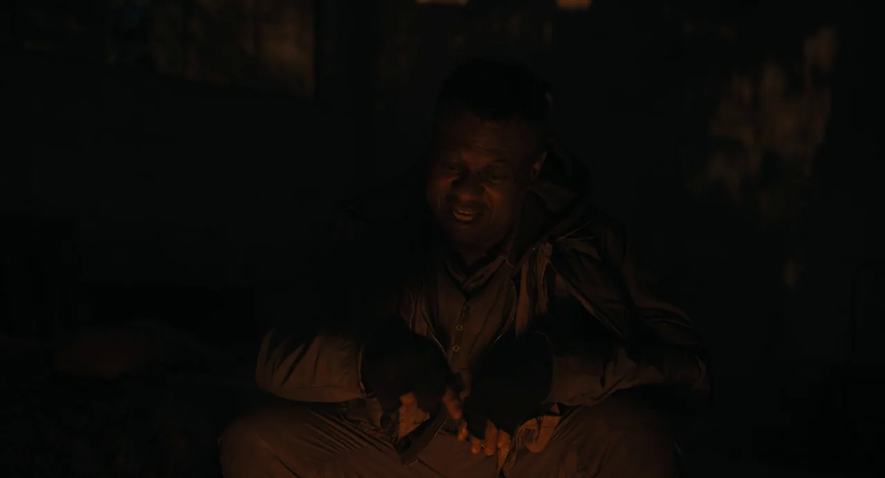Barbarian (2022) movie still: medium — A dimly lit, dark space with indistinguishable surroundings obscured by shadow. A man sits in the dark and…
